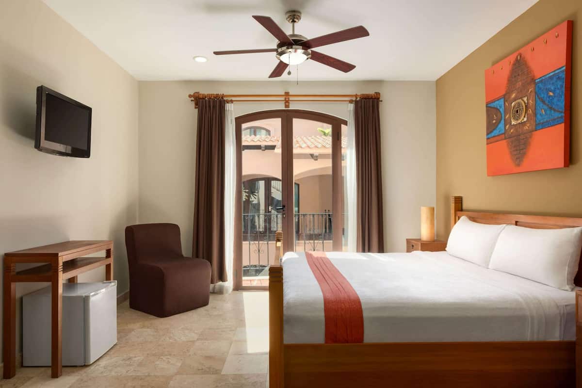 Habitación de hotel con cama, una silla, un escritorio, televisor y balcón con vistas.