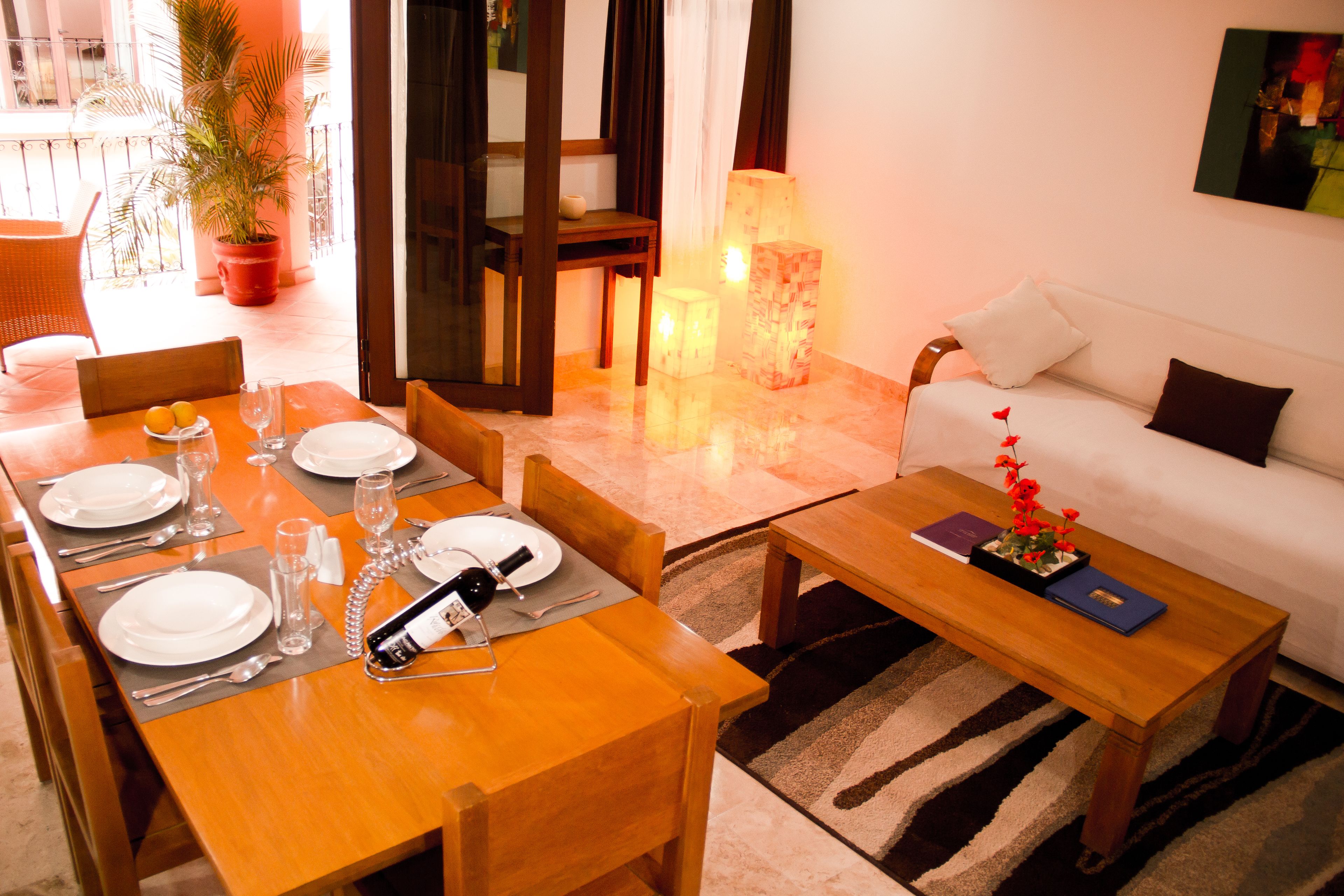 A dining area with a wooden table set for four, a sofa, and a lamp.