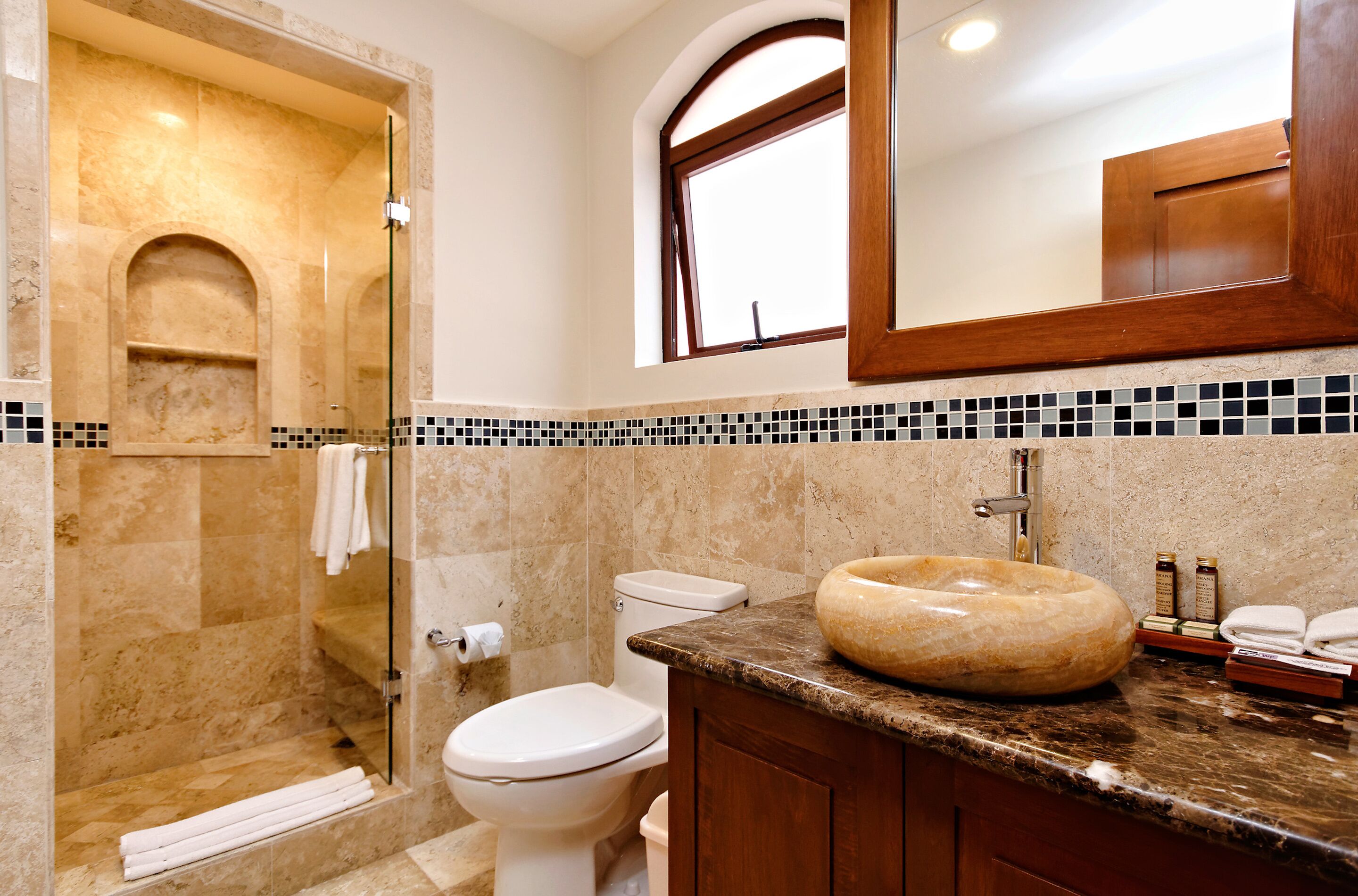 A bathroom with a glass-enclosed shower, a toilet, a sink with a marble countertop, and a mirror above the sink.