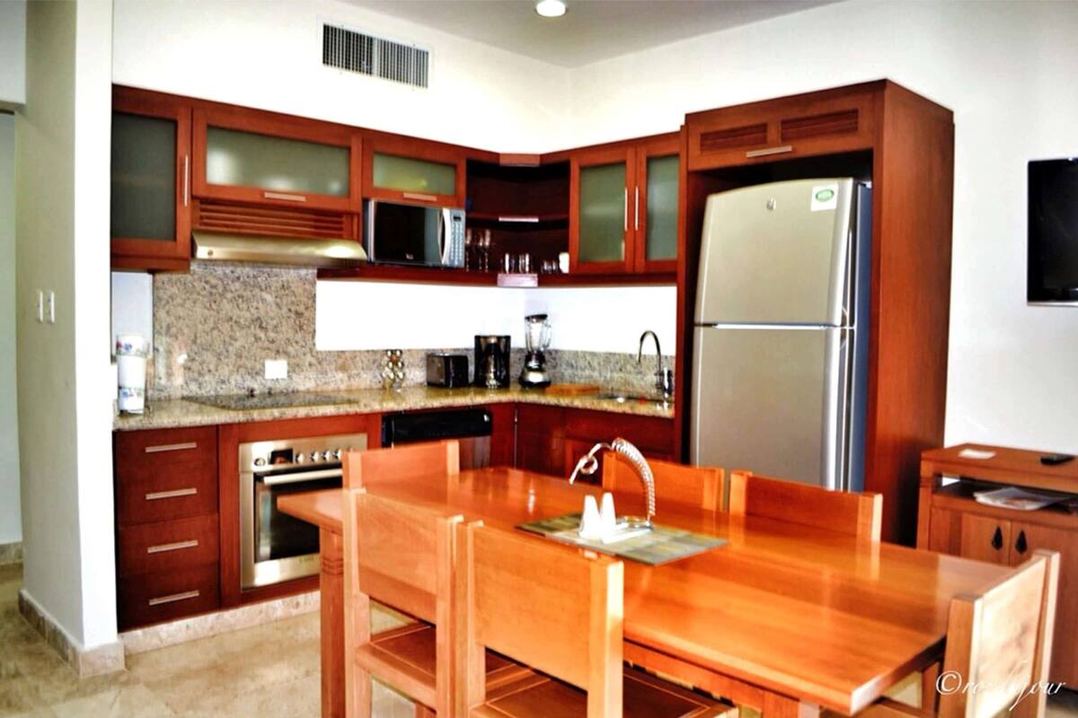Una cocina moderna con encimeras de granito, electrodomésticos de acero inoxidable, armarios de madera y un comedor con mesa y sillas de madera.