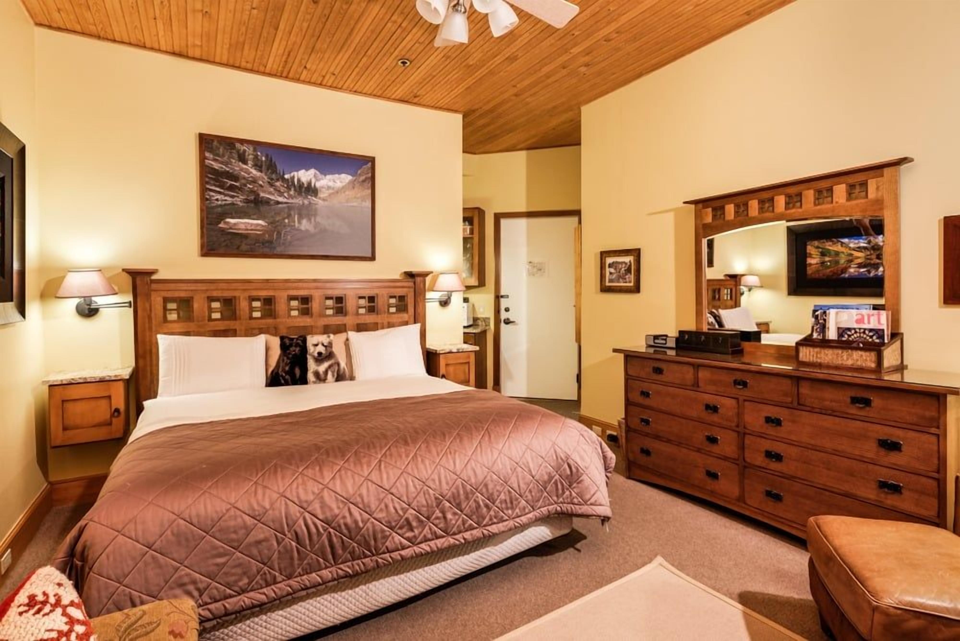 A hotel room with a large bed, wooden headboard, a dresser, a television, and a painting on the wall.