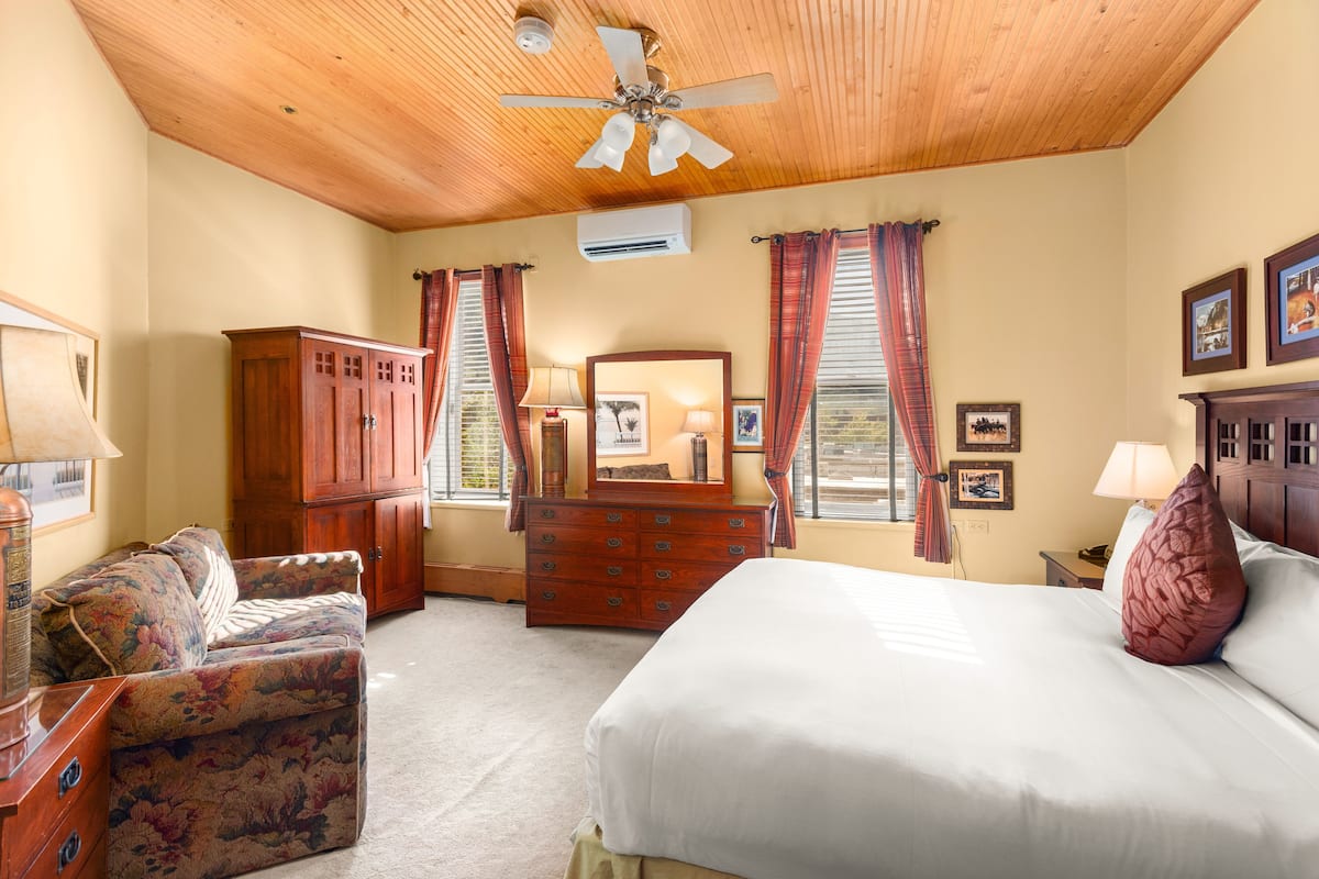 A bedroom with a bed, a wooden ceiling, a dresser, a mirror, and a window with curtains.