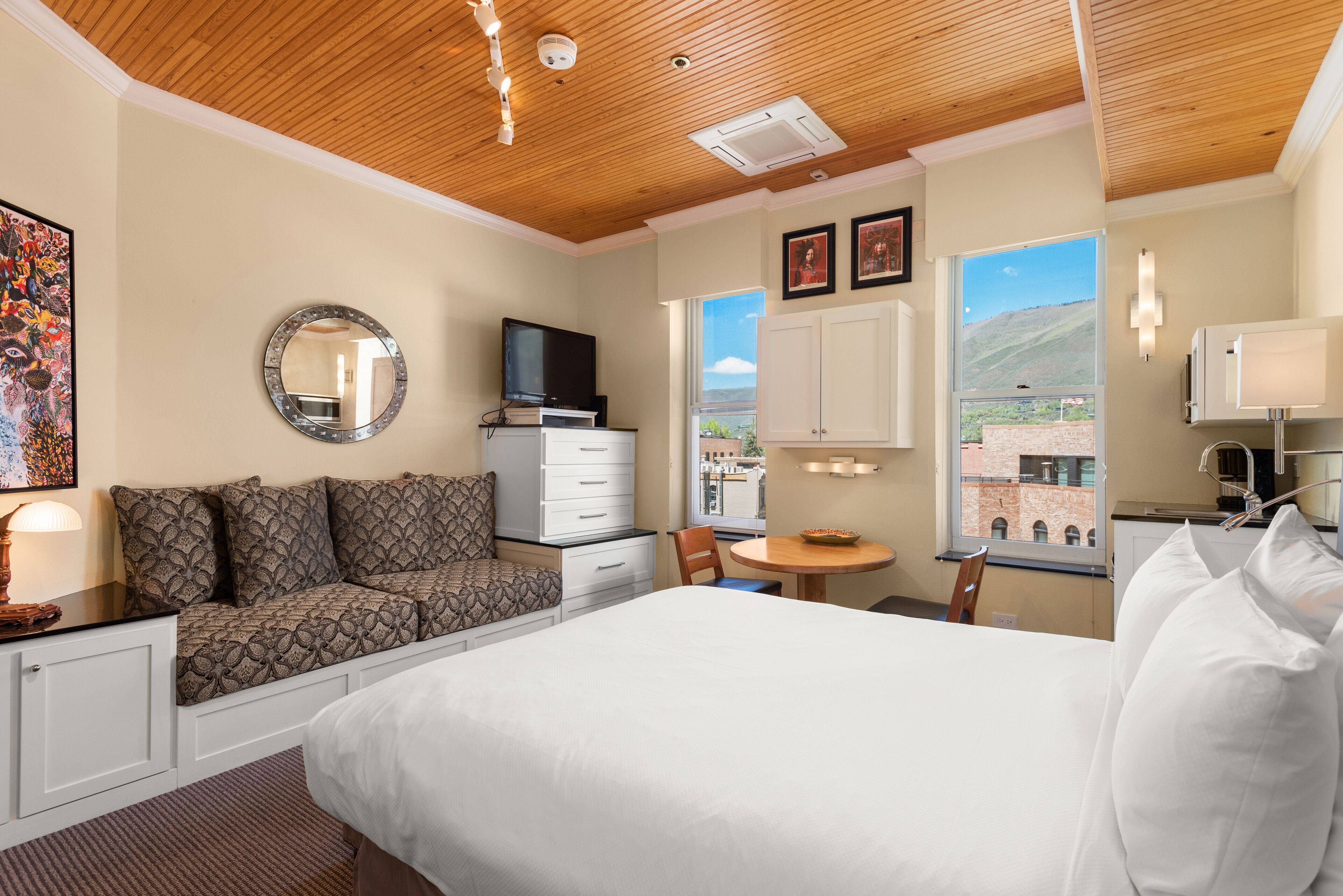 Quarto de hotel com cama, área de estar com TV, mesa de jantar e vista para uma montanha.