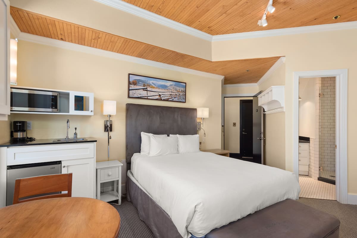 A hotel room with a bed, a desk with a microwave, a chair, and a painting on the wall.