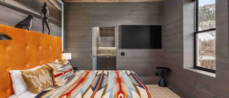 Un dormitorio con una cama grande, techo de madera, un ventanal amplio y televisor instalado en la pared.