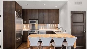 A modern kitchen with dark wood cabinets, stainless steel appliances, and a wooden dining table with four white chairs.