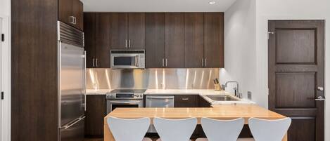 A modern kitchen with dark wood cabinets, stainless steel appliances, and a wooden dining table with four white chairs.