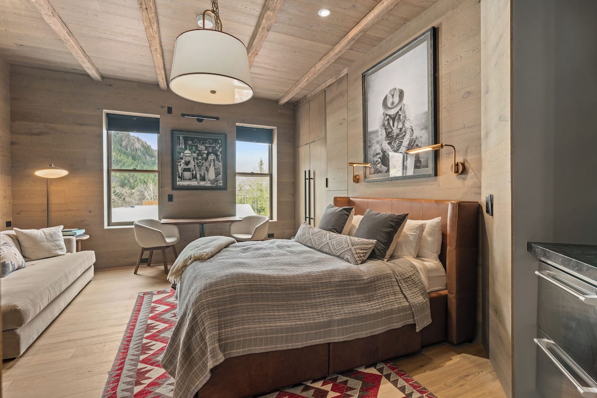 A modern bedroom with a large bed, a desk, and a view of the outdoors.