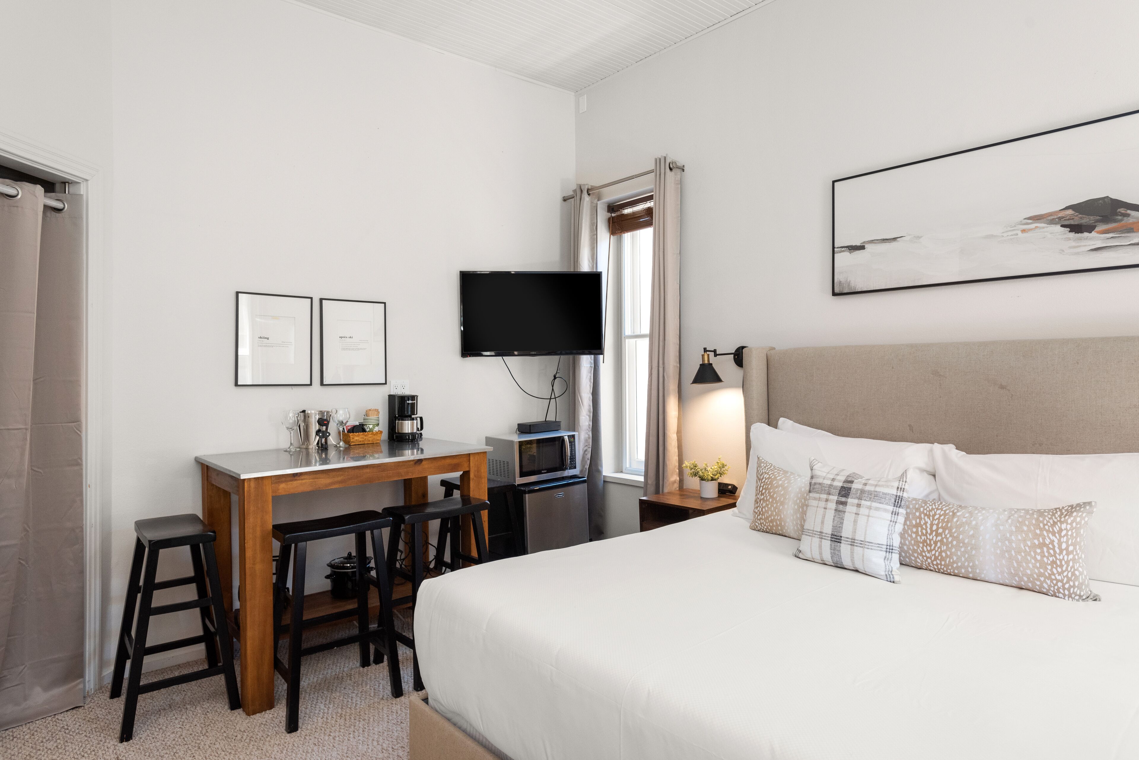 A bedroom with a bed, a desk with a computer, a TV, and a window with curtains.