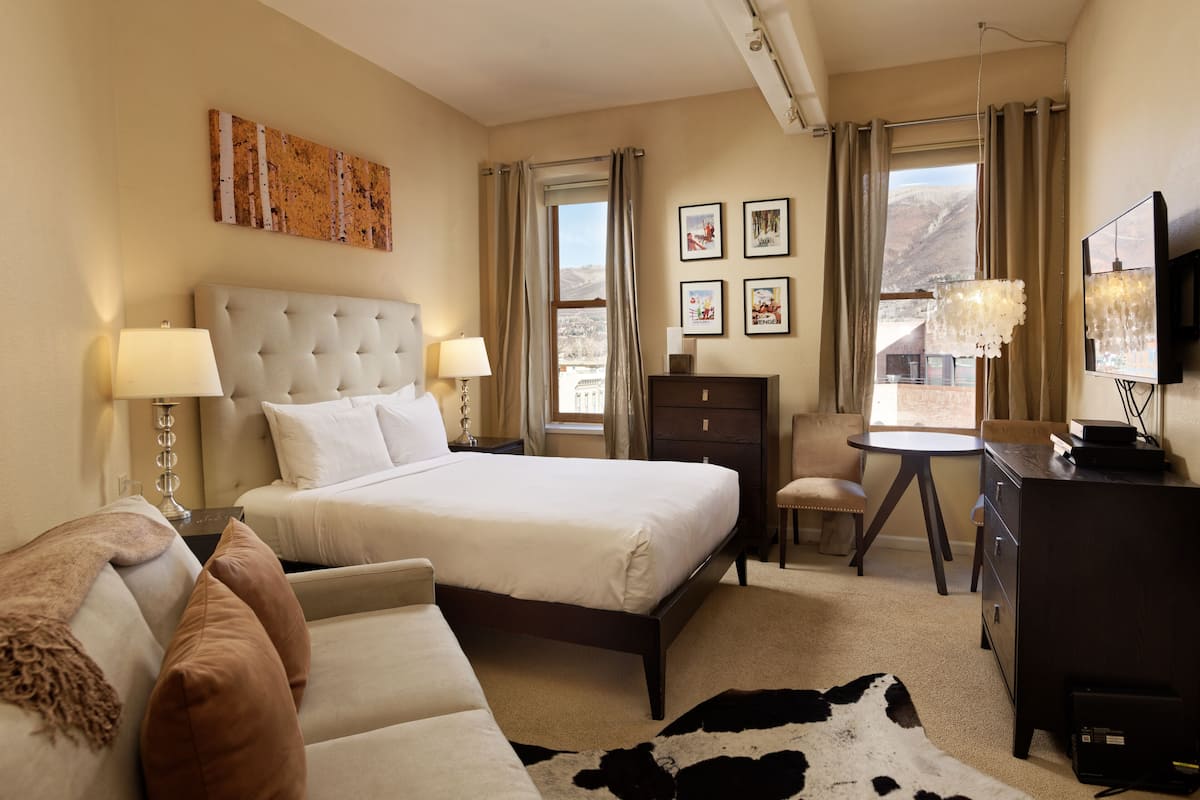 A hotel room with a large bed, a sofa, a desk, a TV, and a view of the mountains.