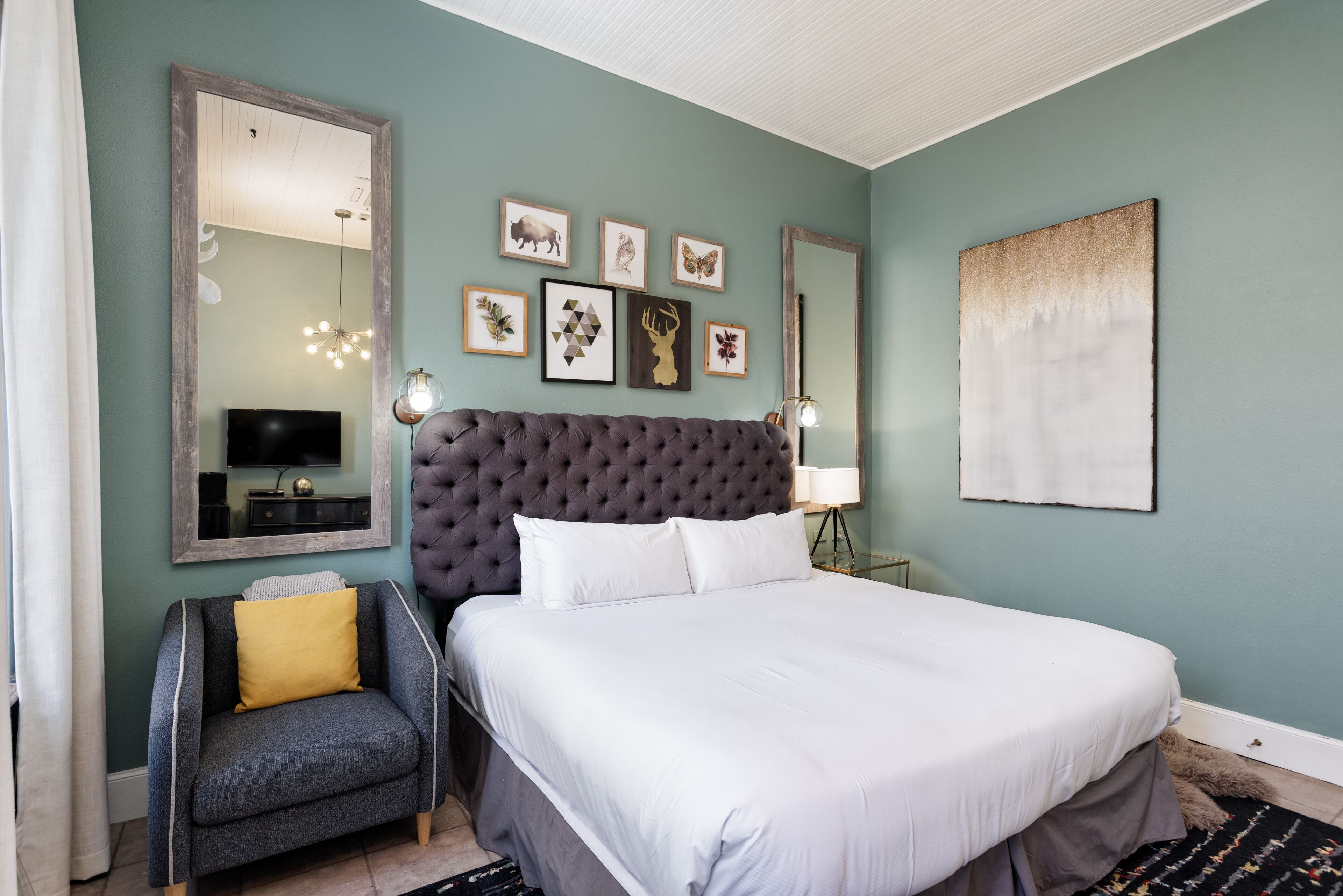 Une chambre à coucher avec un grand lit, un petit canapé, une télévision et des œuvres d’art murales.