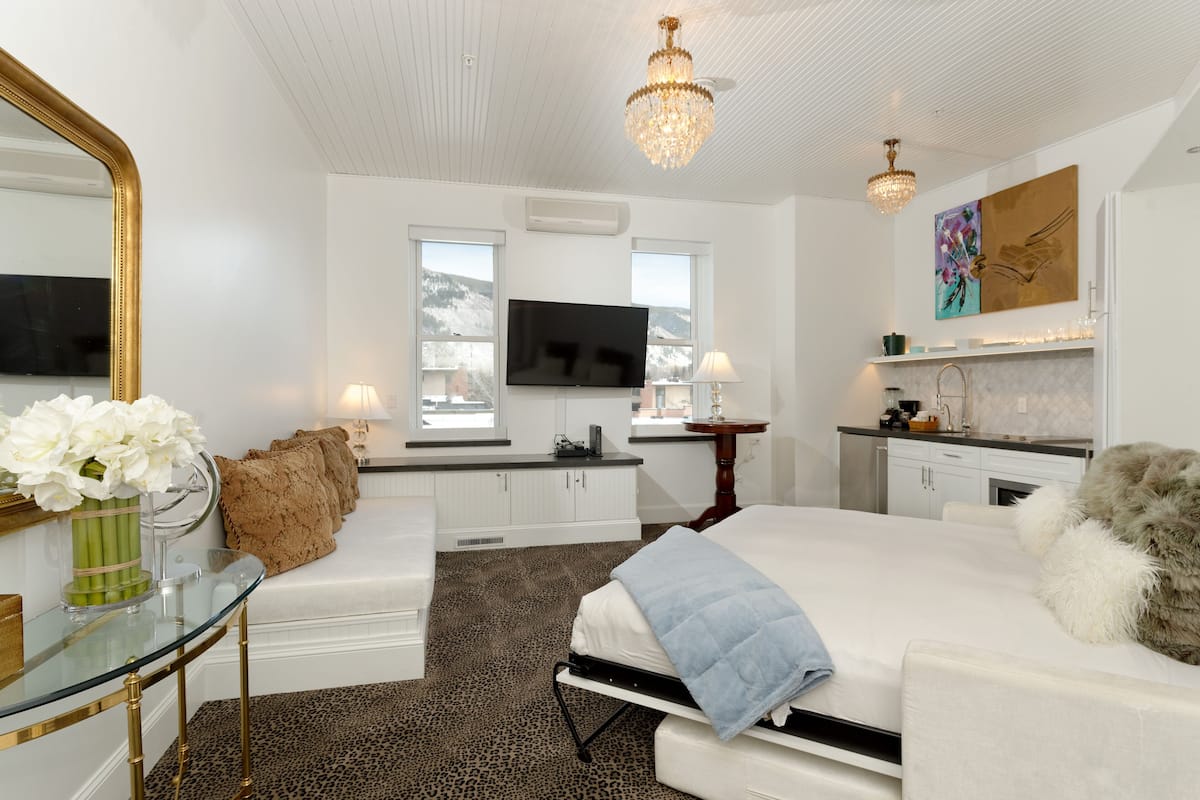 A modern bedroom with a large bed, a glass table, a sofa, a TV, and a chandelier.