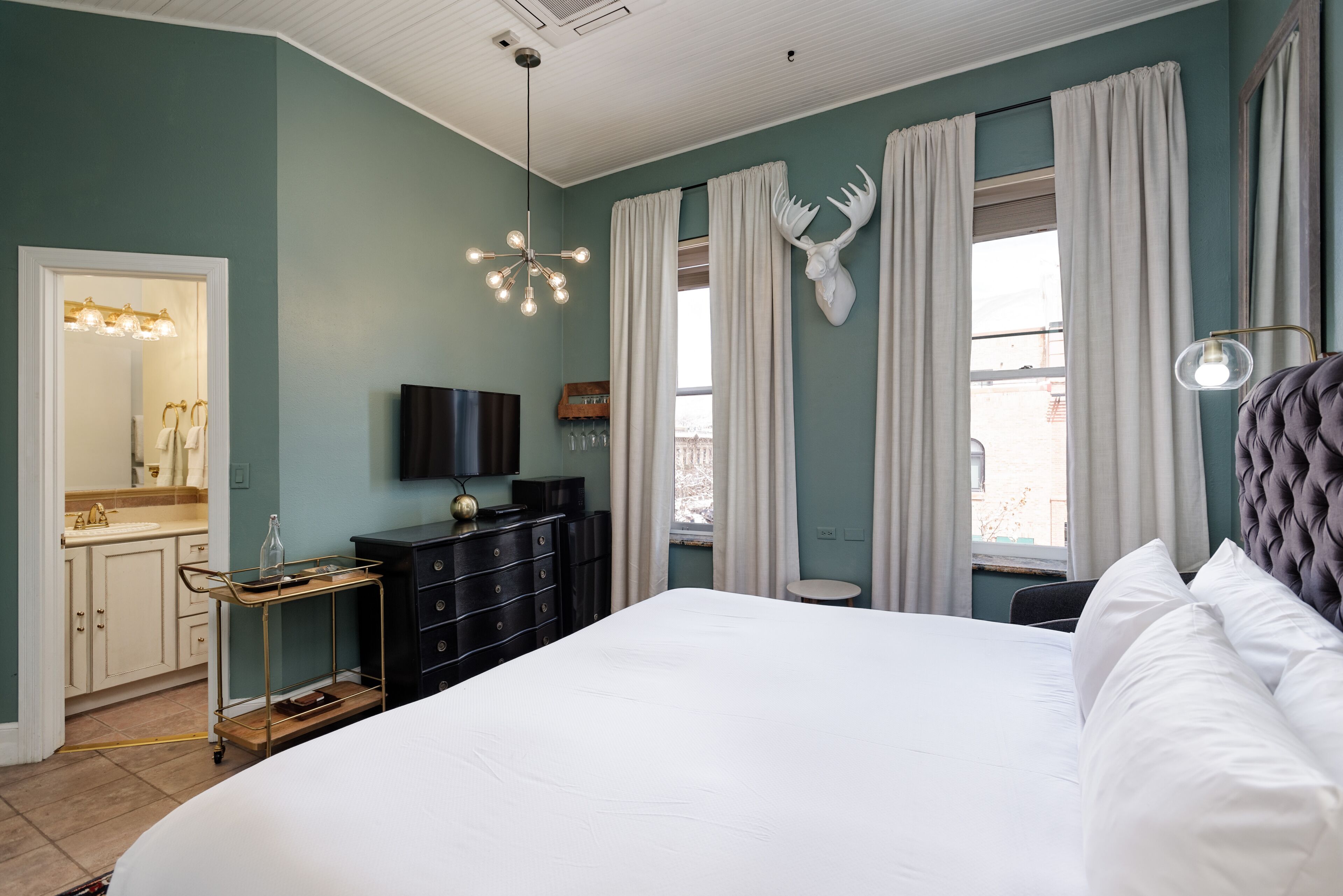 Une chambre à coucher avec un grand lit, une commode, une coiffeuse avec un miroir et un téléviseur fixé au mur.