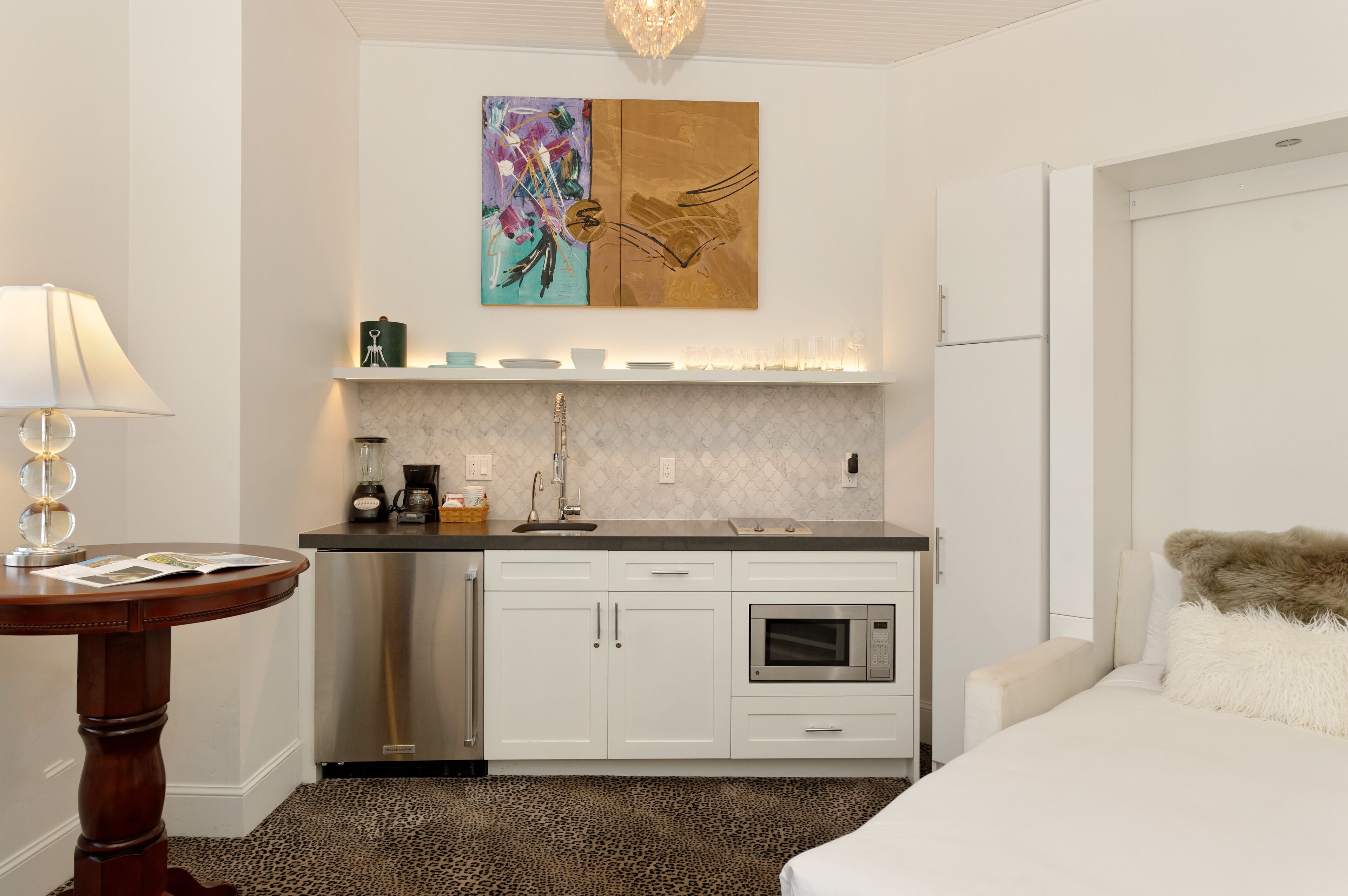 Une chambre d’hôtel moderne équipée d’une kitchenette, d’un lit avec un oreiller moelleux, d’une machine à café et d’un tableau au mur.