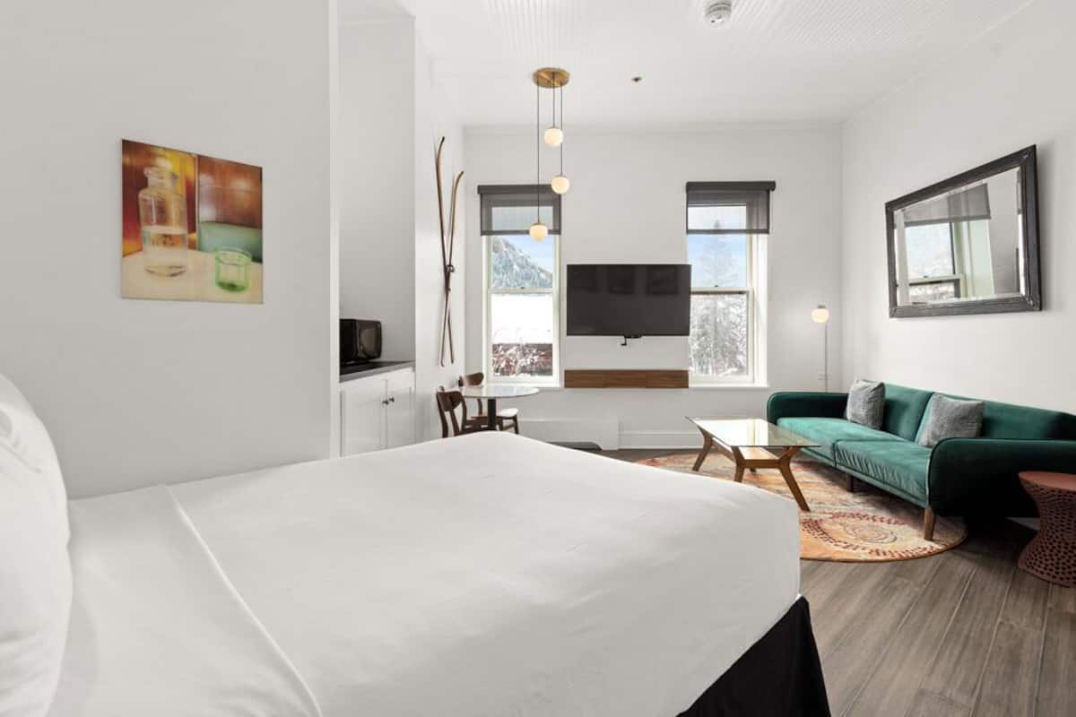 A modern bedroom with a large bed, a green sofa, a TV, and a dining area.