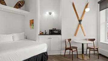 A hotel room with a bed, a small kitchenette, a dining area with a table and chairs, and a wall-mounted ski rack.