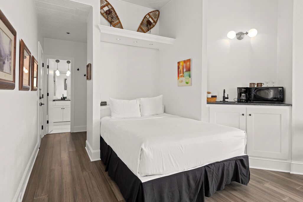 A bedroom with a bed, a kitchenette with a microwave, and a hallway leading to a bathroom.