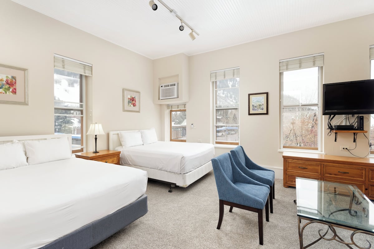 A hotel room with two beds, a desk, a chair, and a TV.
