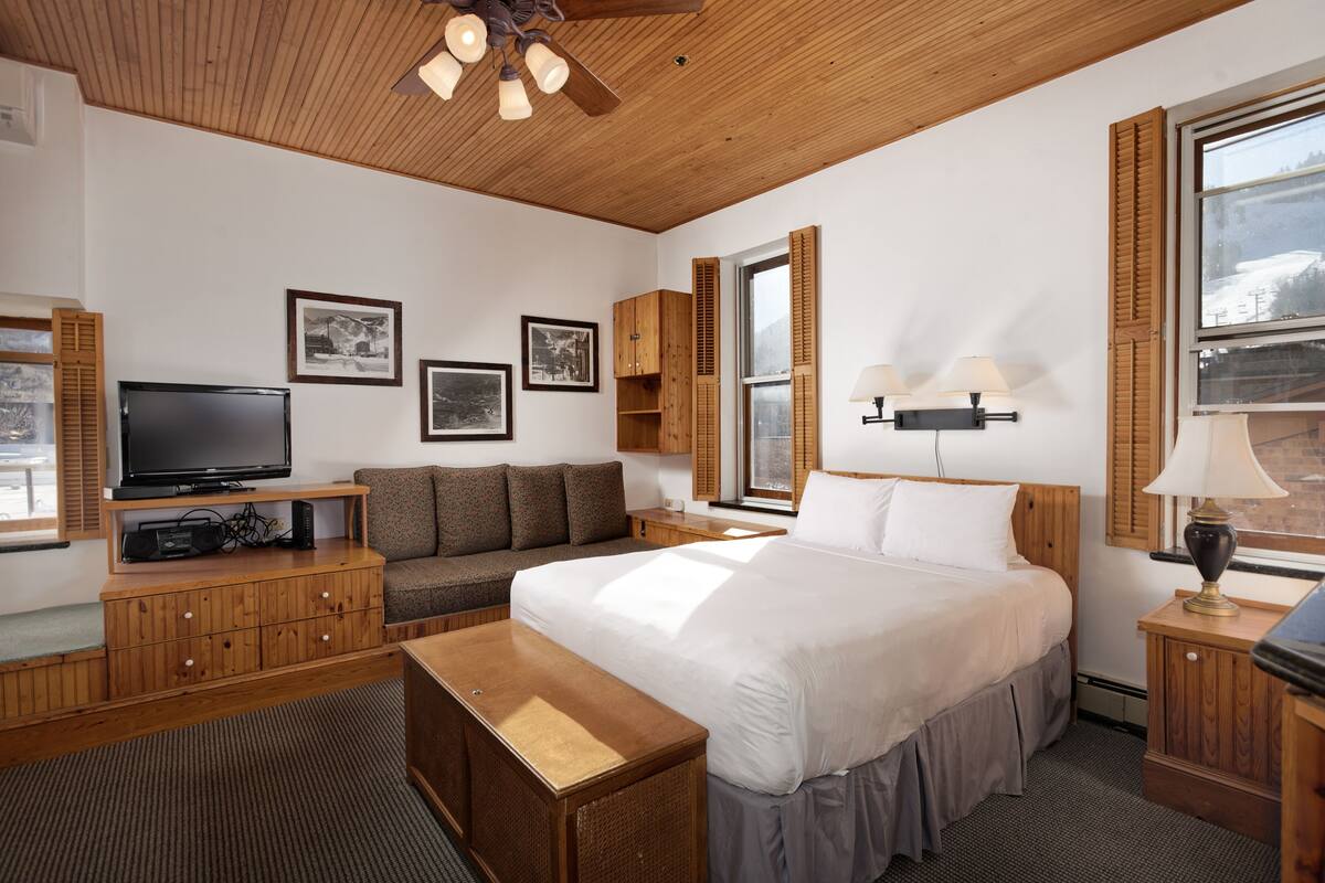 A hotel room with a bed, a TV, a sofa, wooden furniture, and framed pictures on the wall.