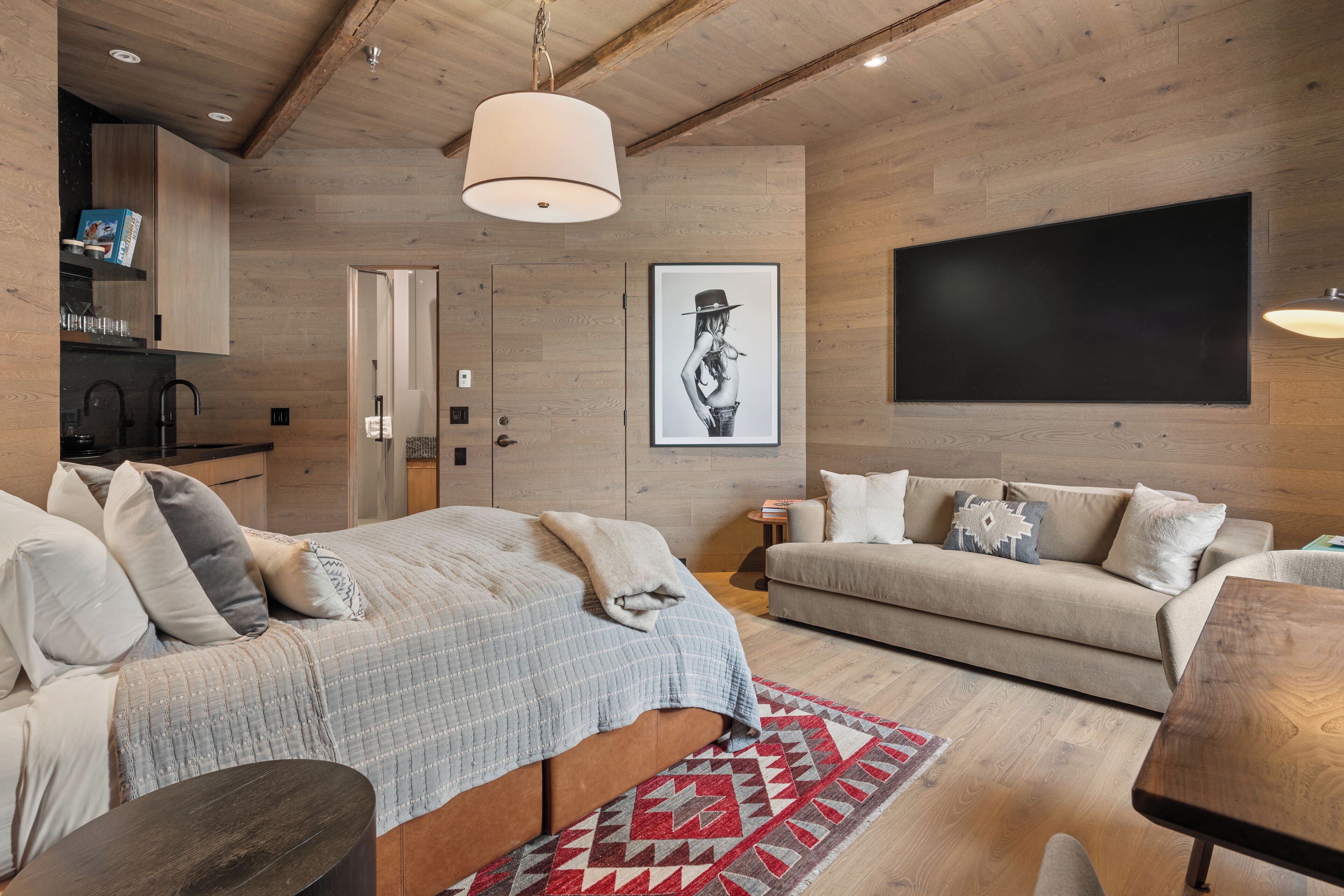 Un dormitorio moderno con una cama, un sofá, techo de madera y un televisor grande.