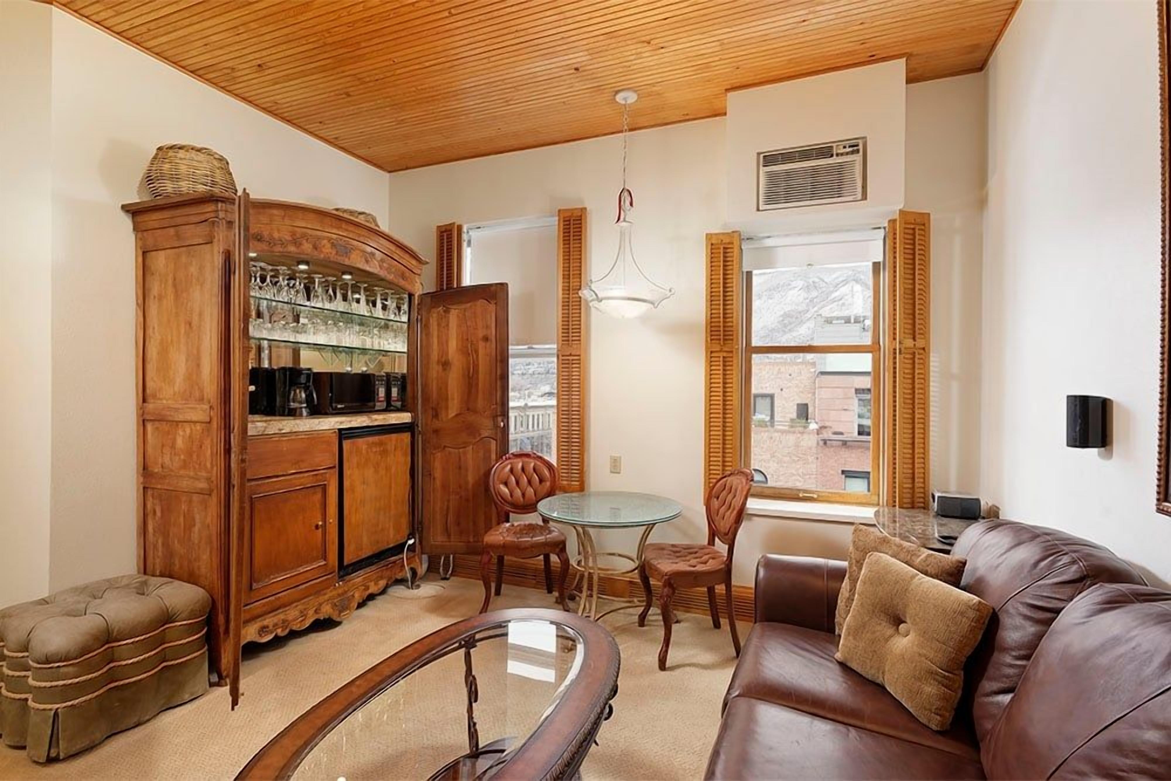 A cozy living room with a wooden cabinet, leather sofa, and a glass table.