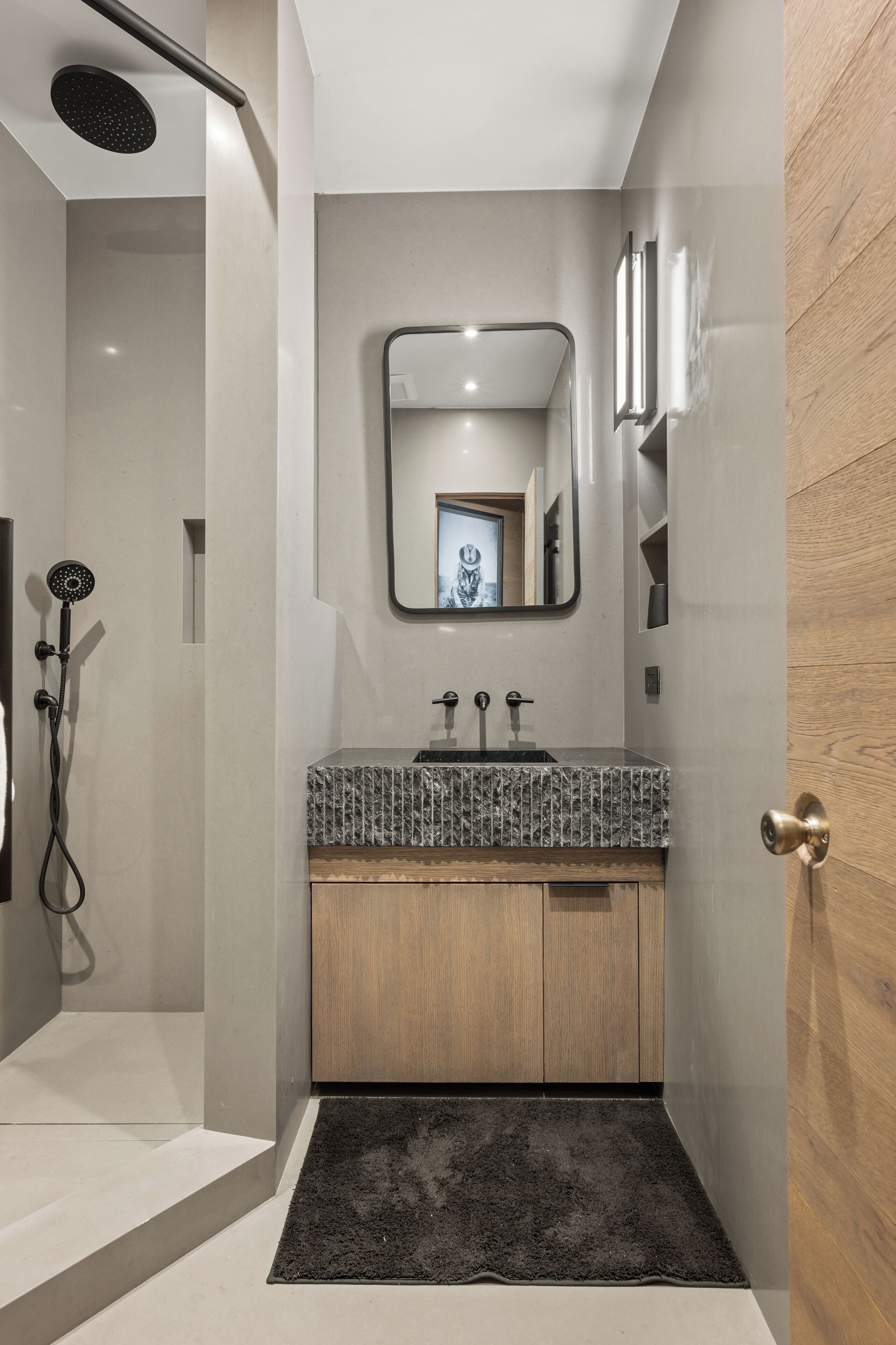 Un baño moderno con ducha, lavamanos con espejo y puerta de madera.