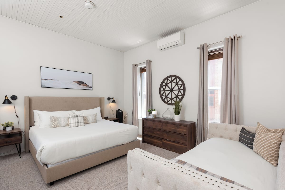 A bedroom with two beds, a dresser, a wall-mounted air conditioner, a framed picture, and a decorative wheel.