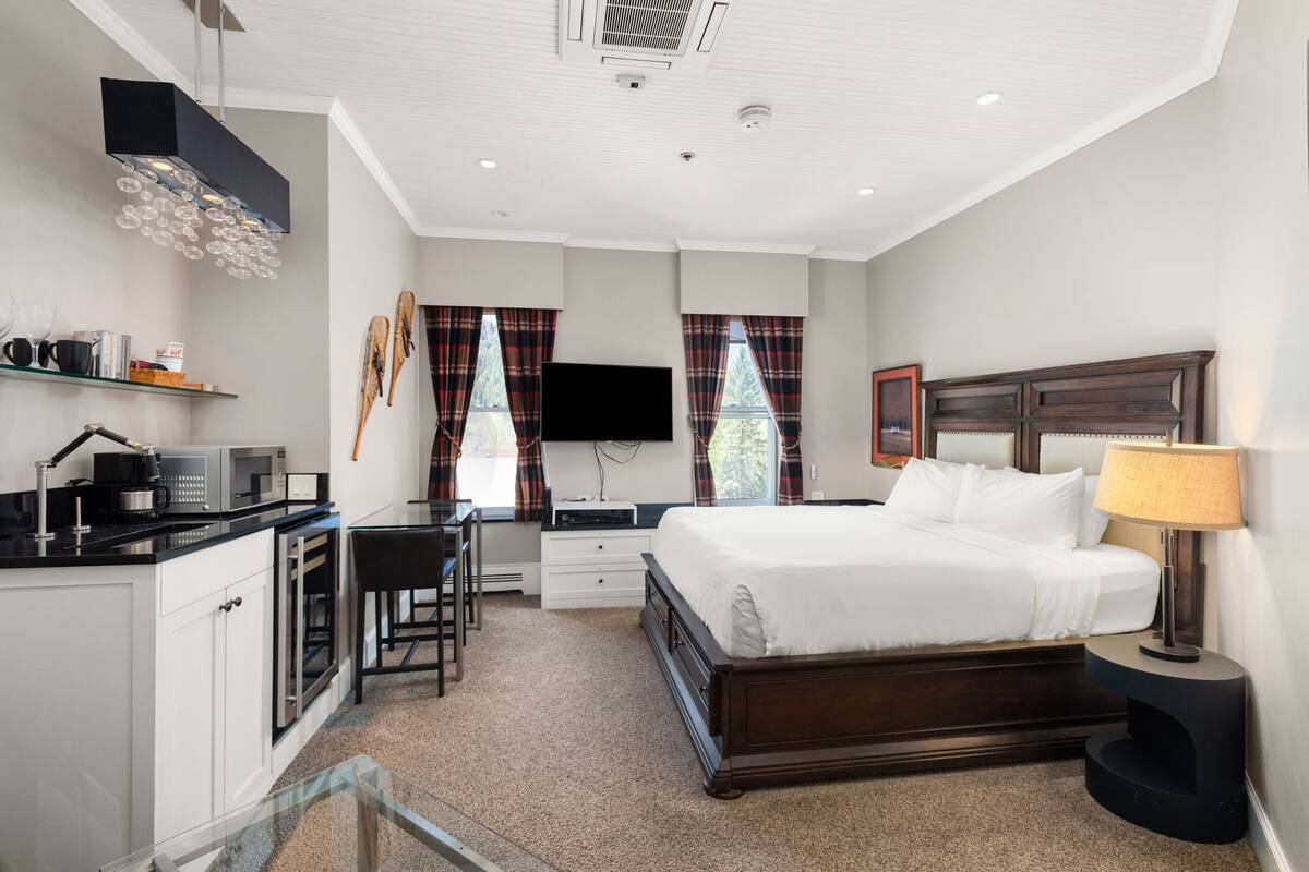 A modern hotel room with a bed, desk, and kitchenette.