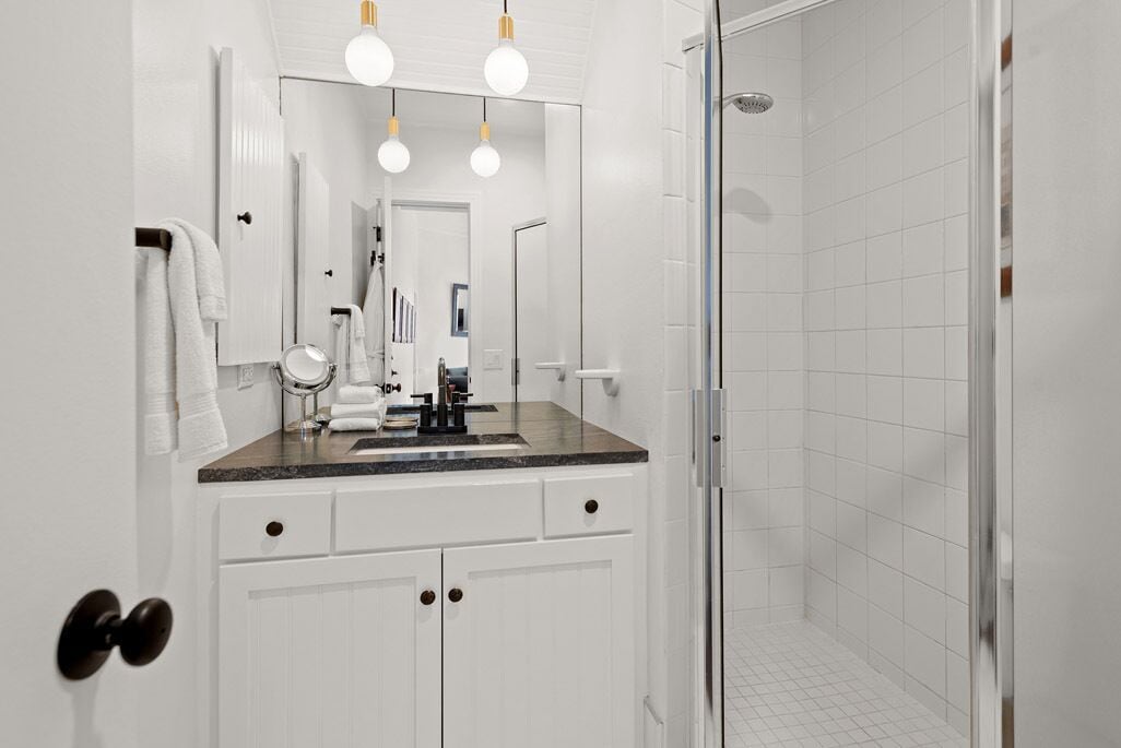 A modern bathroom with a white vanity, a glass shower enclosure, and a mirror with lights above.