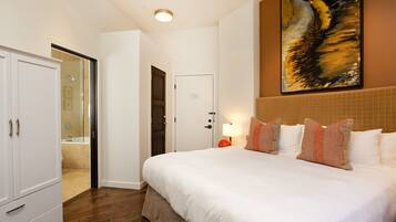 Habitación de hotel con una cama grande, un armario, un baño con puerta de cristal y un cuadro en la pared.