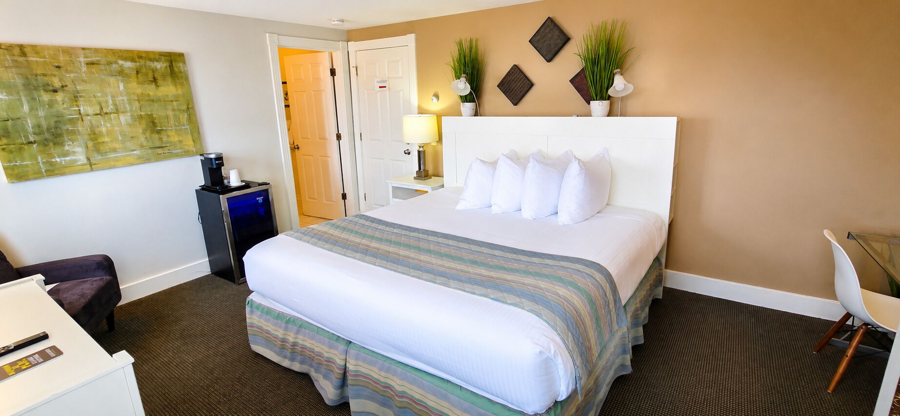 Habitación de hotel con cama, escritorio, silla, cafetera y lámpara de pared.