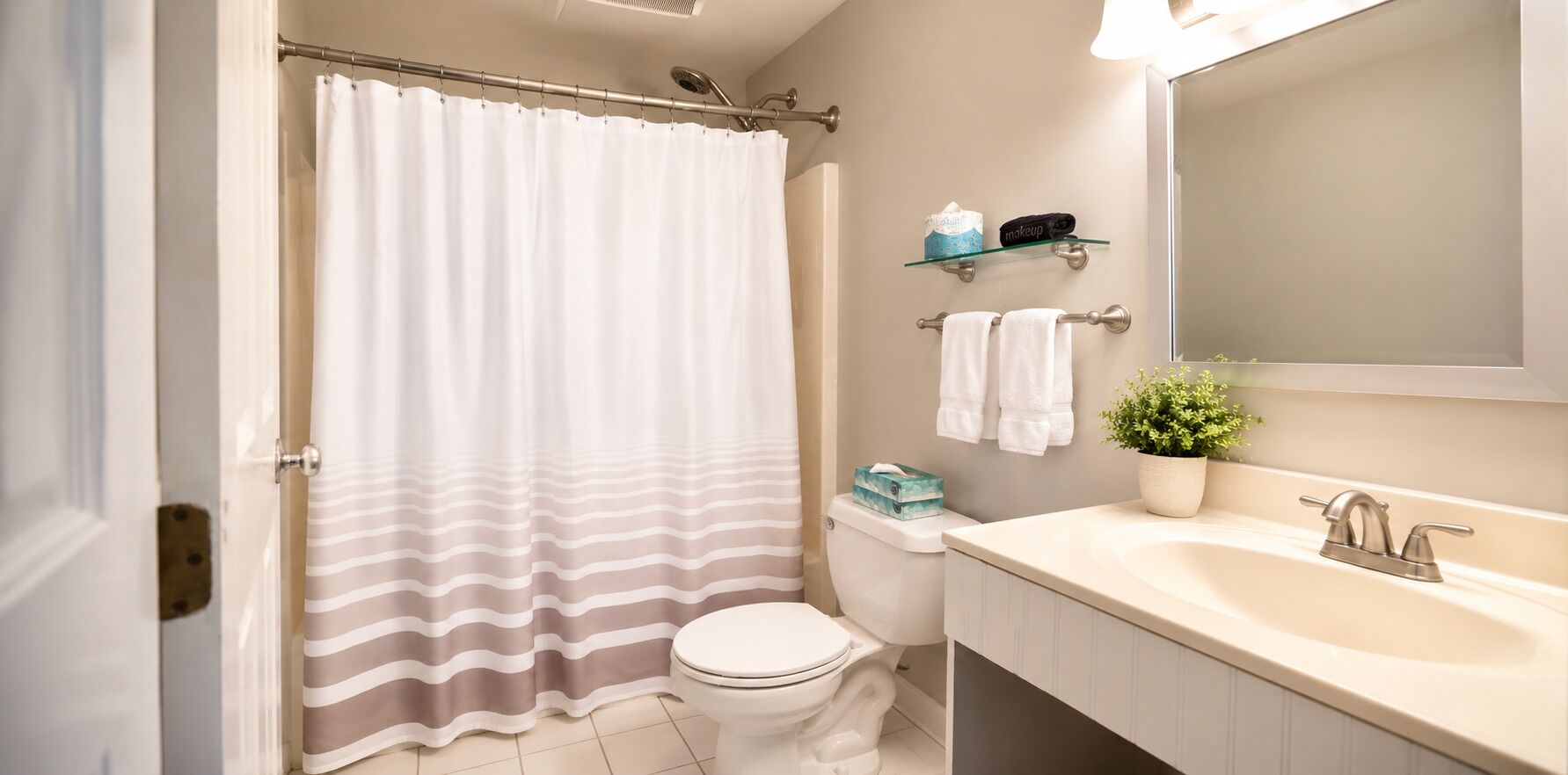 Un baño con cortina de ducha, inodoro, lavabo, espejo y repisa con artículos de aseo.