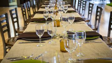 Una larga mesa de comedor dispuesta con varios vasos de vino, cubiertos y platos, rodeada de sillas.