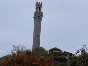 A tall stone tower with a narrow window near the top, surrounded by trees with autumn leaves. - Pilgrim House (Provincetown)