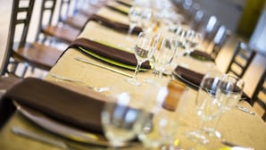 A dining table set with wine glasses and cutlery, arranged in a row with chairs on either side.