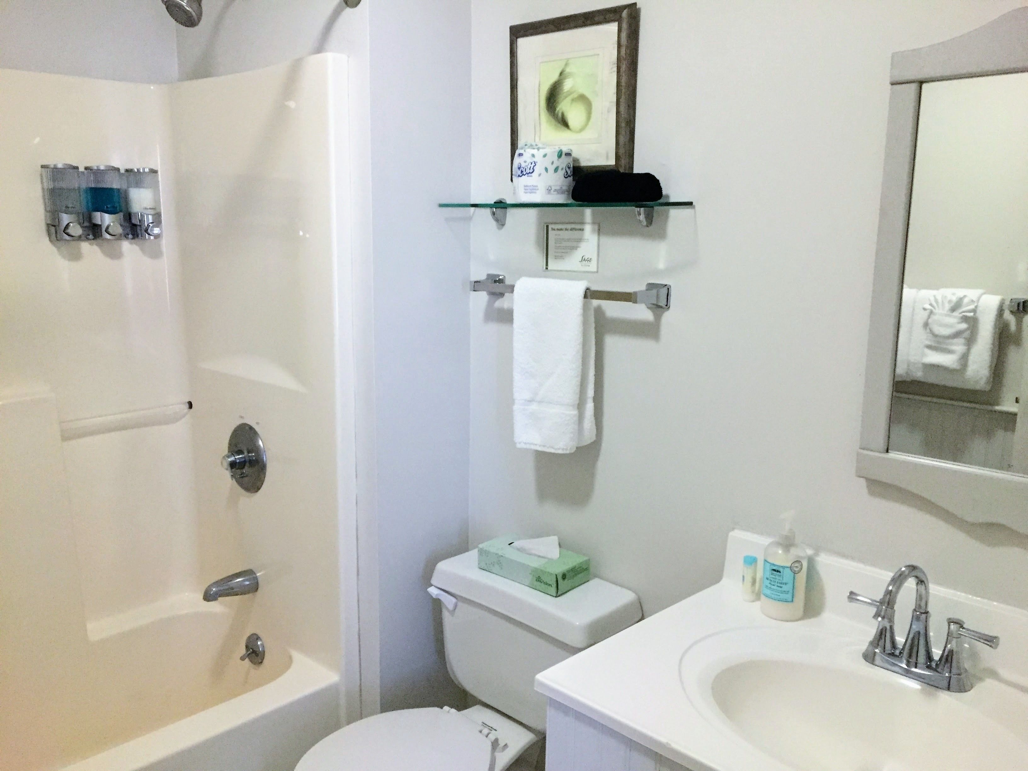 A bathroom with a bathtub, toilet, and sink. There are toiletries on the wall and a towel hanging on the wall.