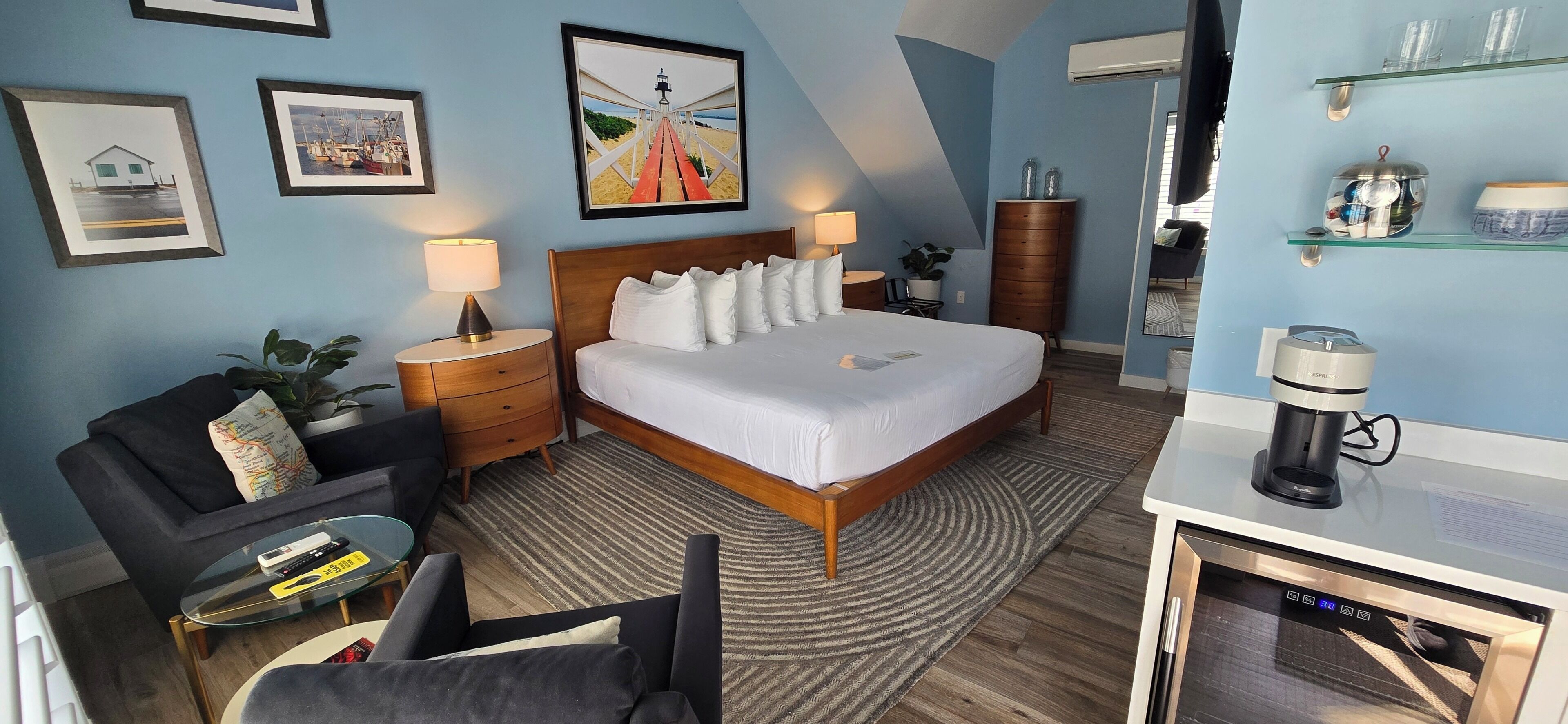 A hotel room with a bed, bedside tables, a desk with a coffee machine, and a TV.