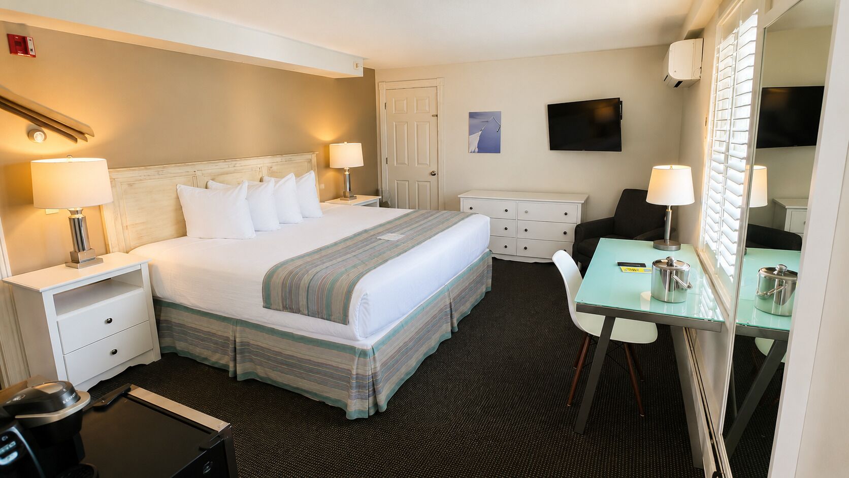 A hotel room with a bed, bedside tables, a desk, a chair, a television, and a mirror.