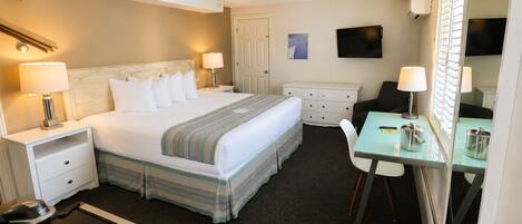 A hotel room with a bed, bedside tables, a desk, a chair, a television, and a mirror.