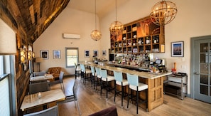 Eine Bar mit einer langen Theke, mehreren Hockstühlen und einer Auswahl an Flaschen und Gläsern.