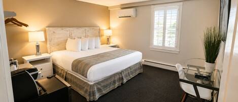 Une chambre d’hôtel avec un lit, des tables de chevet, un bureau, une chaise, une fenêtre et une plante en pot.