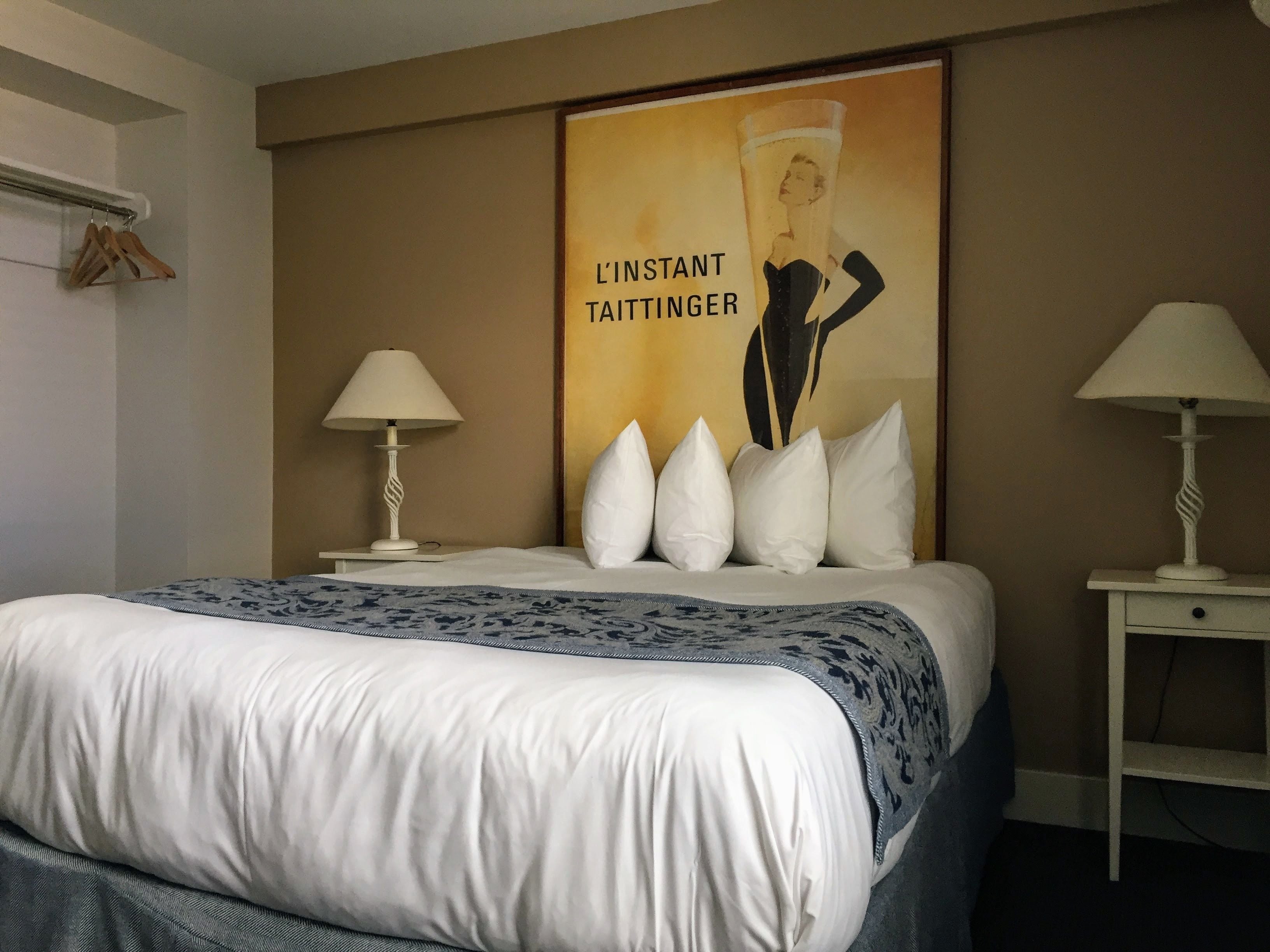 A neatly made bed with a patterned throw, two bedside lamps, and a poster on the wall.