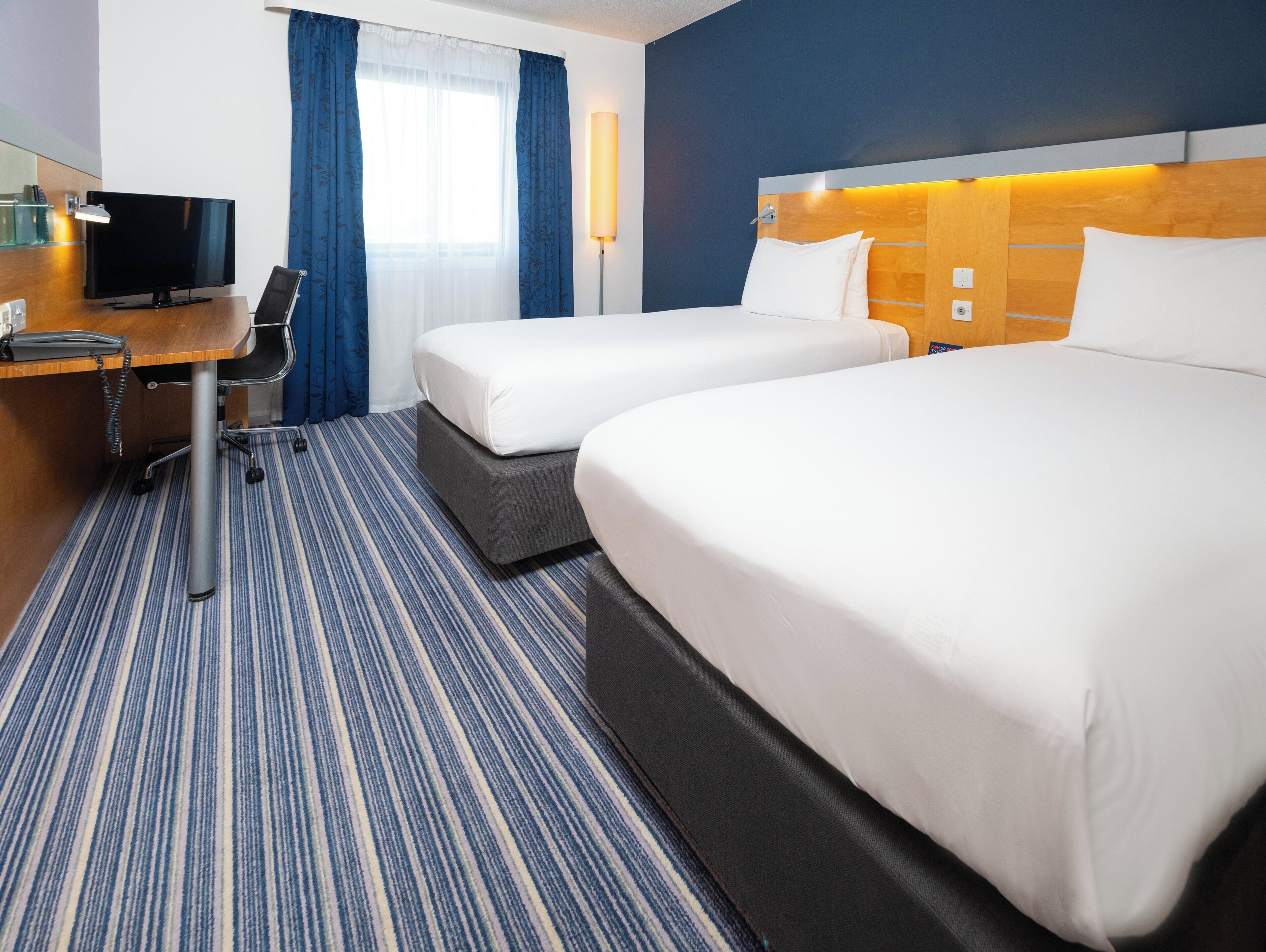 A hotel room with two beds, a desk with a computer, a TV, and a lamp.