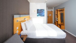 A modern hotel room with a large bed, a wooden headboard, a bedside table, a wardrobe, and a wall-mounted artwork. - Holiday Inn Express Stevenage by IHG (Stevenage)