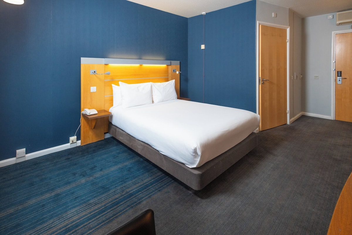 A hotel room with a bed, bedside table, and a desk.