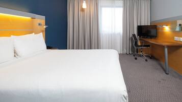 Camera d'albergo con un letto grande, una scrivania con una sedia, una televisione e una finestra con tende.