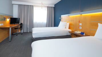 Een hotelkamer met twee bedden, een bureau met stoel, een televisie en een telefoon op het nachtkastje.