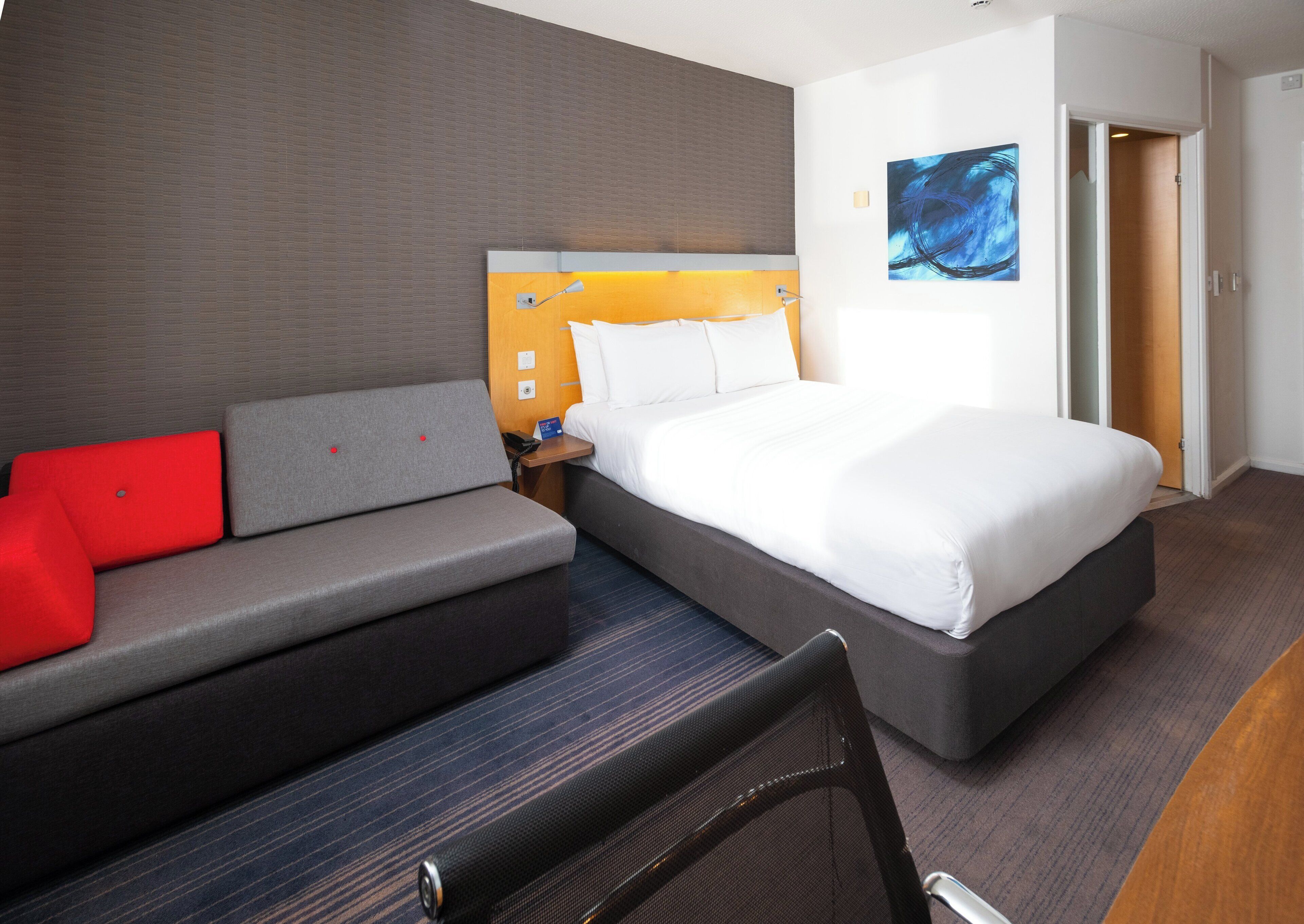 Ein Hotelzimmer mit Bett, Sofa, Schreibtisch und einem Gemälde an der Wand.