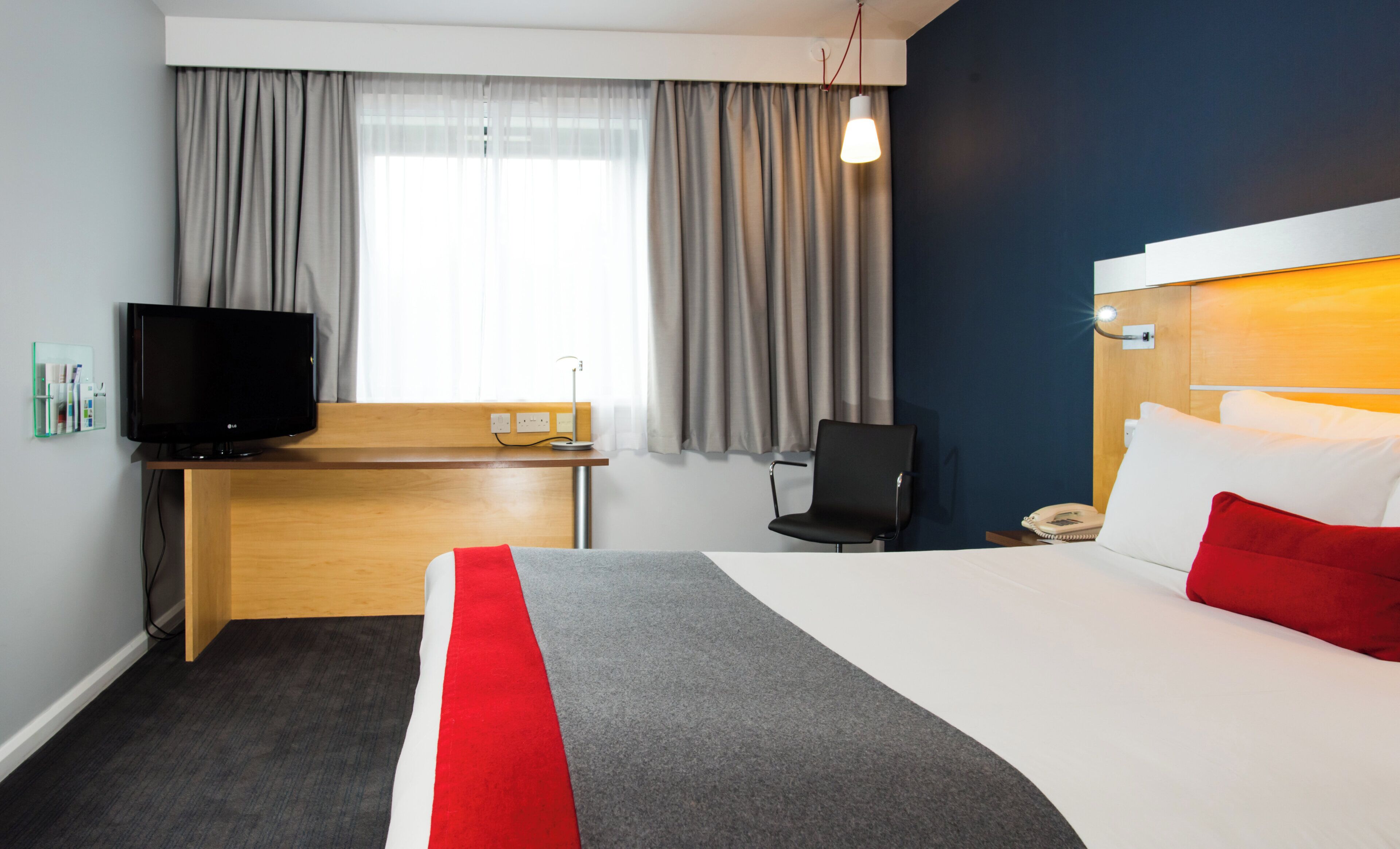 A hotel room with a bed, a desk, a television, a chair, and a telephone.