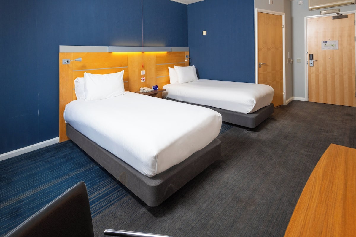 A hotel room with two beds, a desk, and a chair.